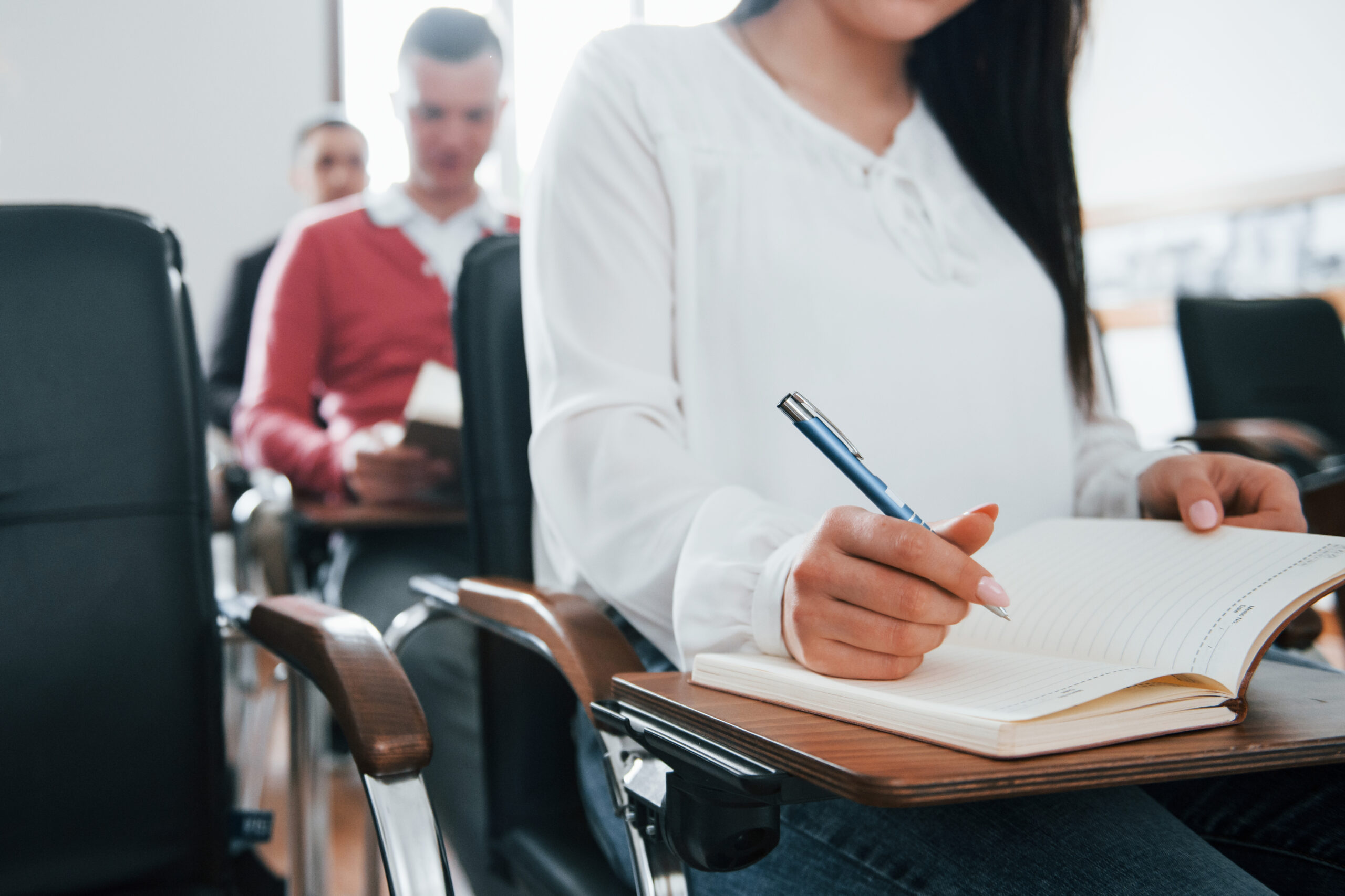 With notepad and pen in hands. Group of people at business conference in modern classroom at daytime.